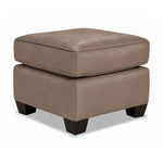 City Leather Ottoman - Stone in a three-quarter view with a thick piped cushion, leather upholstery and dark wood legs