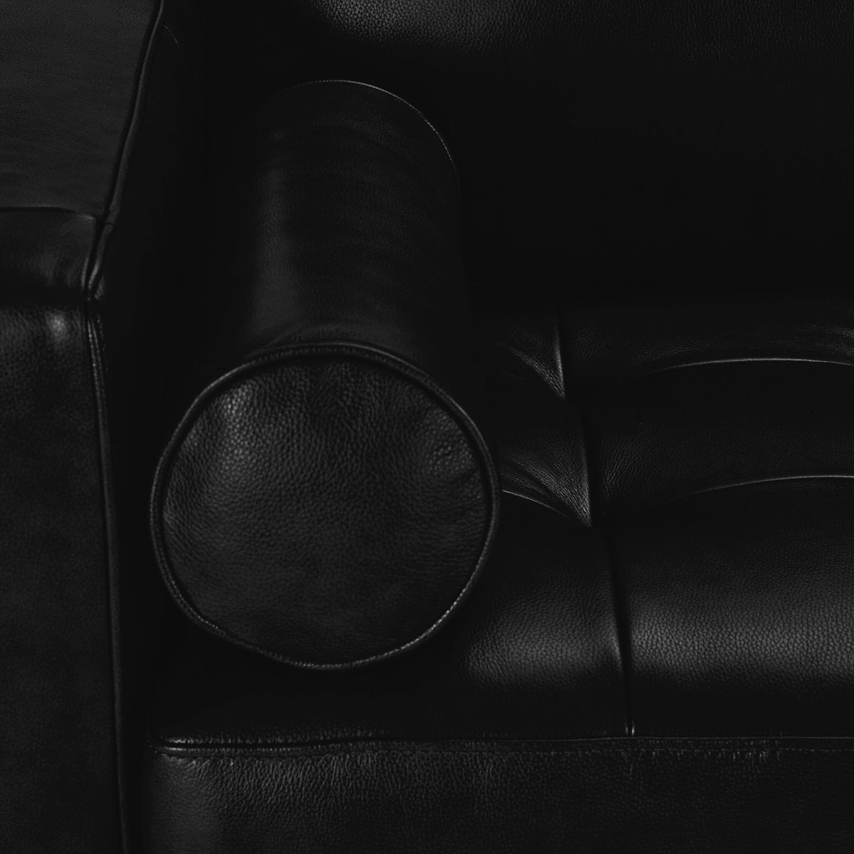 Close-up of black Bari Loveseat showing leather upholstery, bolster pillow and tufted seat cushioning.
