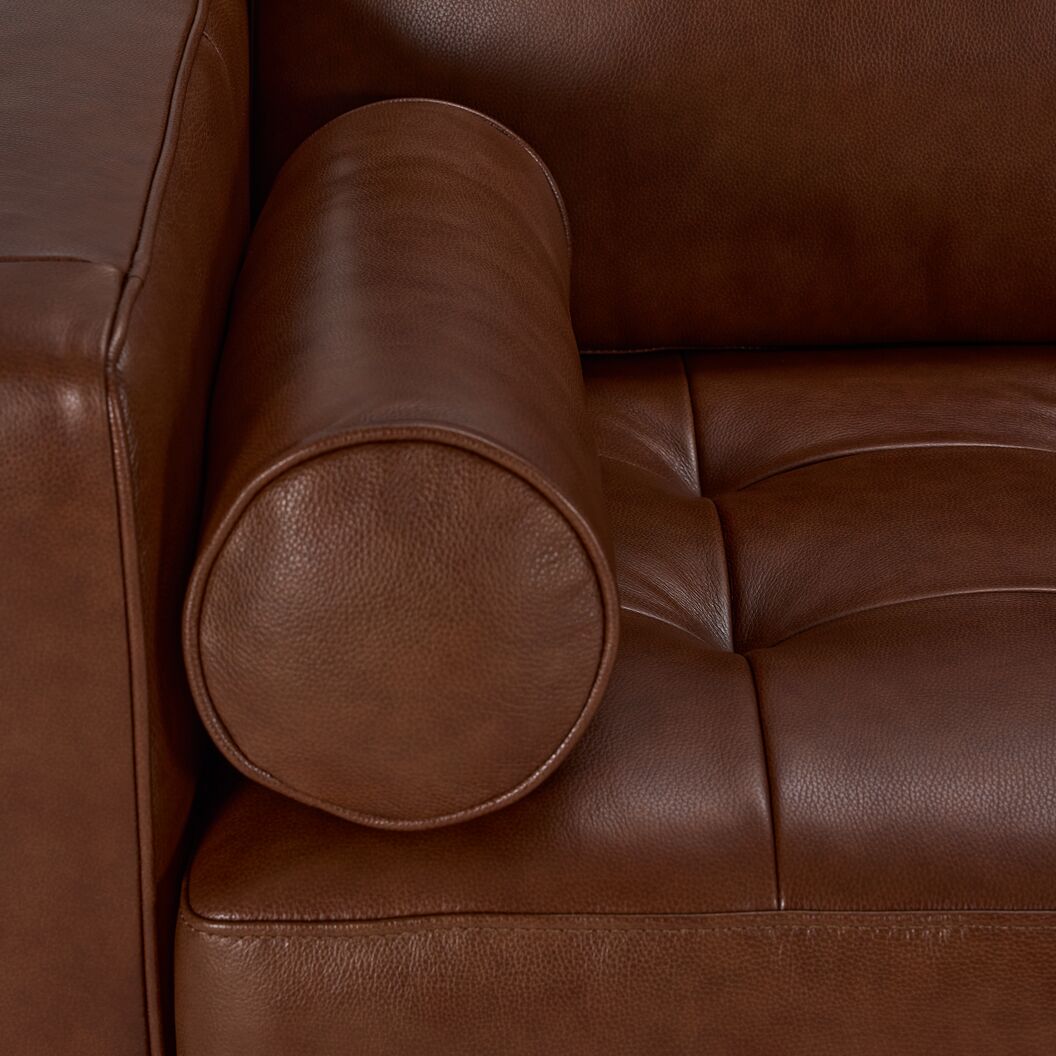 Close-up of the Bari Leather Loveseat showing cobblestone brown leather, cylindrical bolster pillow and tufted seat stitching
